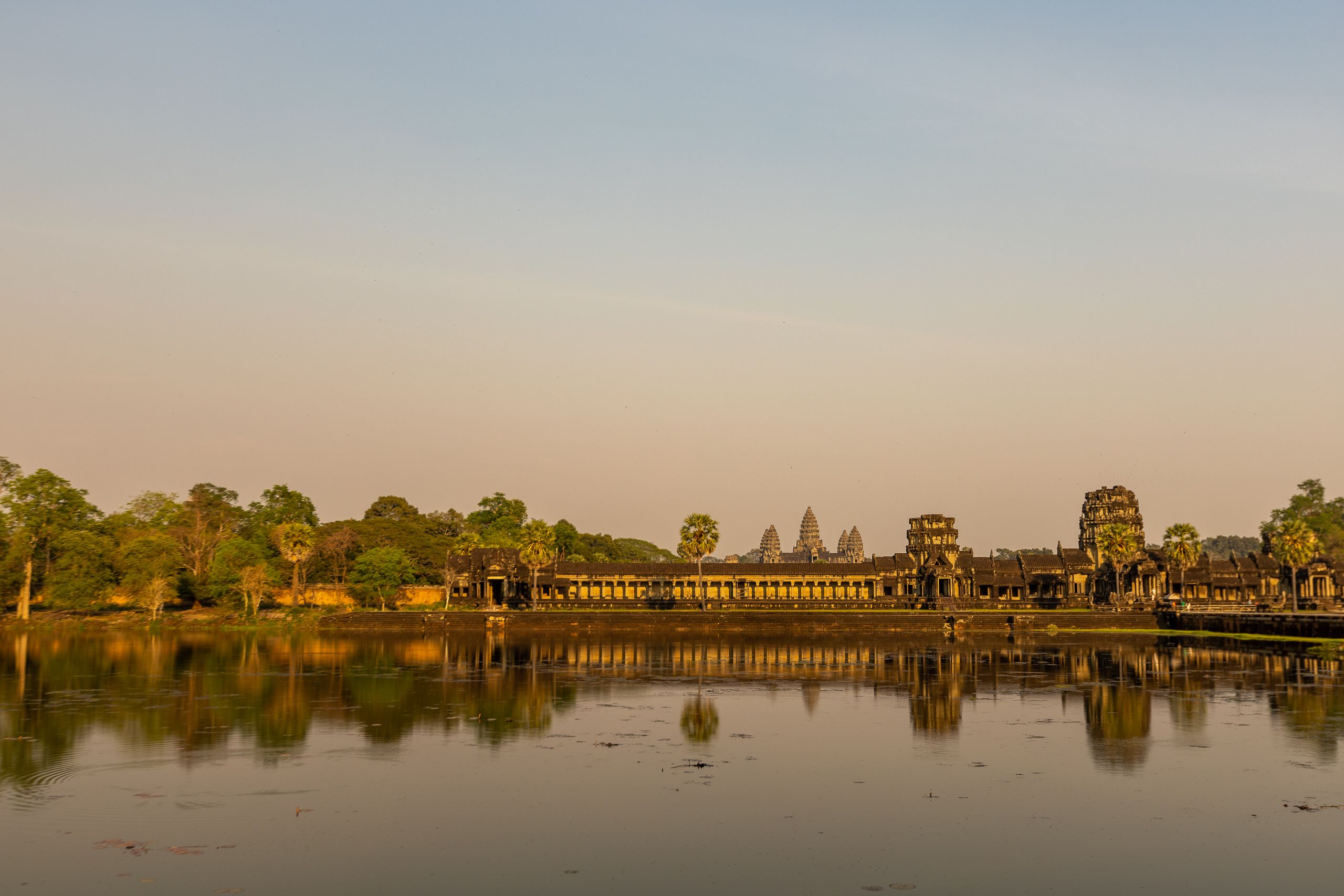 Majestic Angkor Wat temple reflecting in calm waters at sunrise, showcasing ancient architecture.
