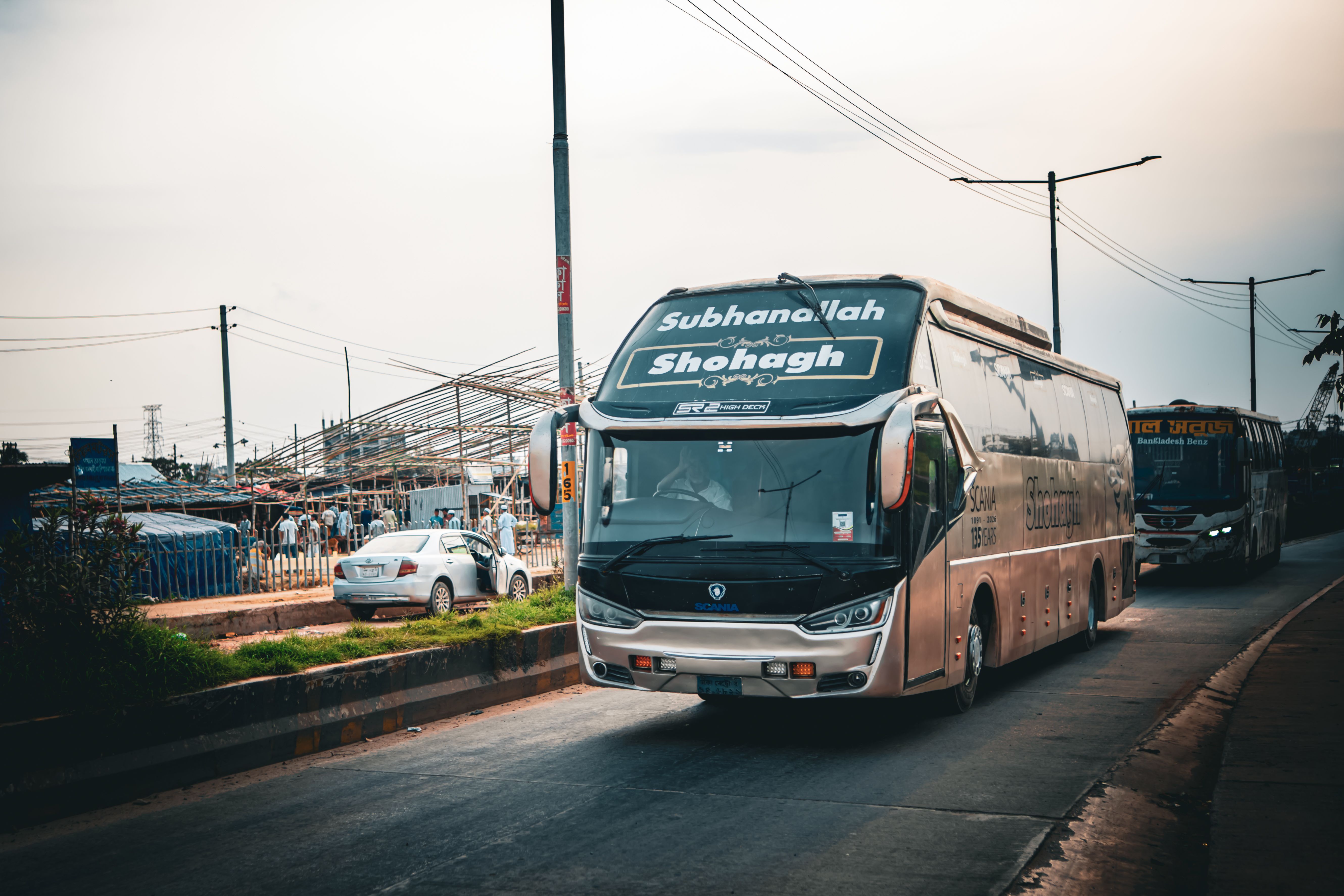 A large city bus travels on a busy road in Dhaka, Bangladesh, under a hazy sky.